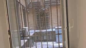 Ein Zimmer mit Fenster zum Innenhof, einem schwarzen Schreibtisch und einem Holzbstuhl.
