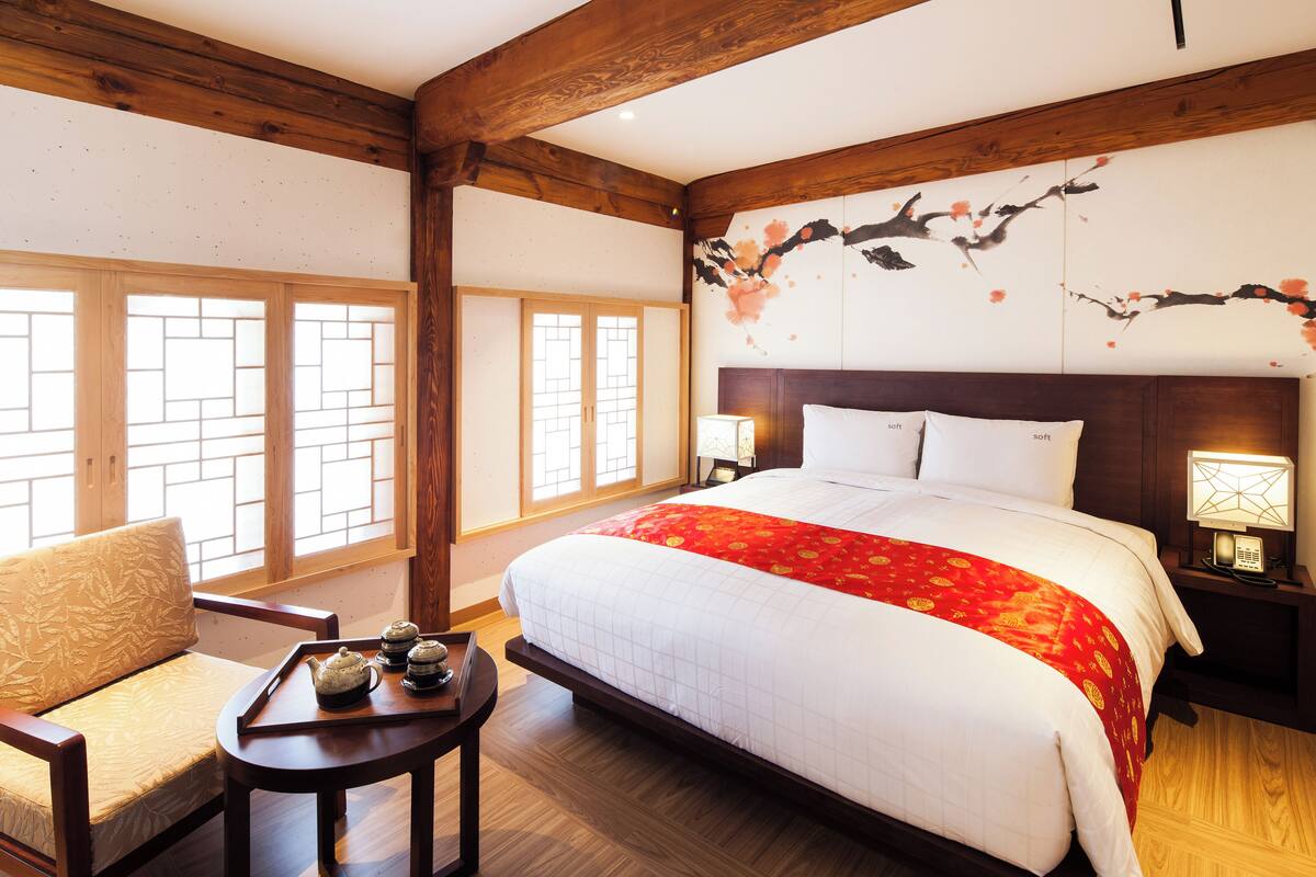 A hotel room with a large bed, a wooden ceiling, a traditional Japanese sliding door, and a small table with a teapot.