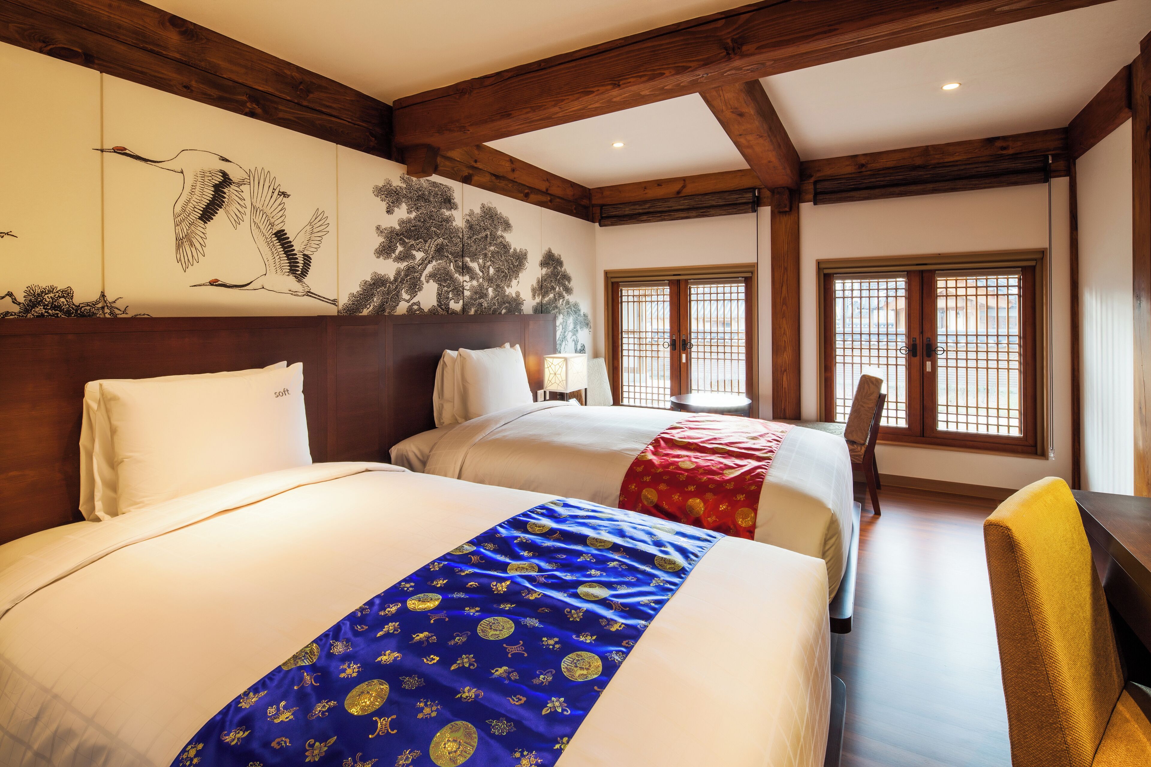 Et hotelværelse med to senge, trælofter og et traditionelt japansk vægmaleri.