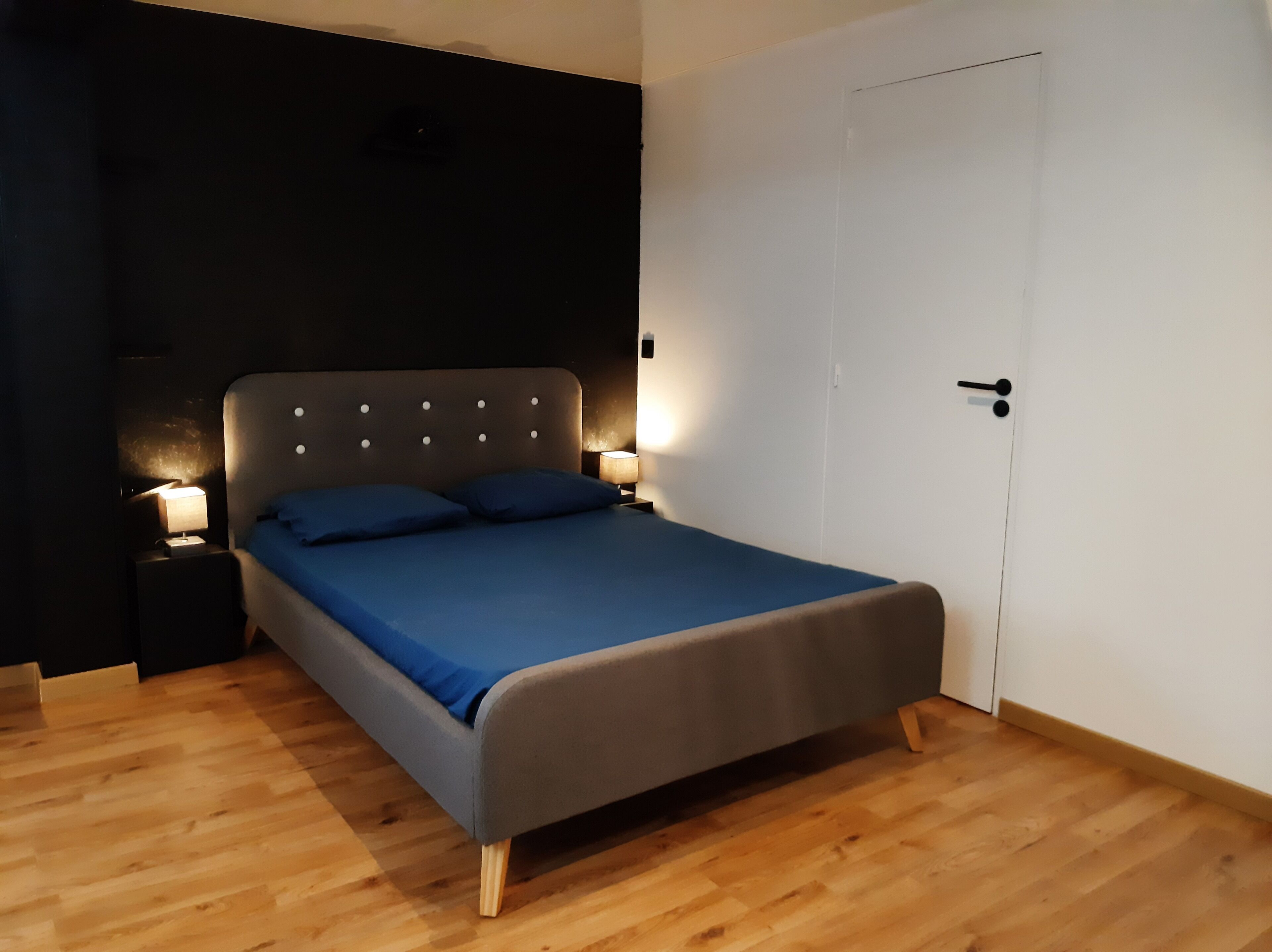 Une chambre à coucher avec un lit, deux tables de chevet avec des lampes, une porte blanche et un plancher en bois.