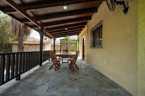 Un portico coperto con pavimento in pietra, arredi in legno e ringhiera in metallo.