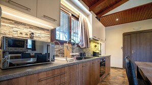 Une cuisine moderne avec un revêtement mural en pierre, des armoires en bois, un grand îlot central doté d’un évier et un coin repas avec une table et des chaises.