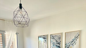 A modern living room with a grey quilted sofa, two framed abstract paintings, a hanging light fixture, and a small wooden table. - NEW! 2 Bedrooms, 2 Bathrooms, Free Car Box 100m from the sea (Alba Adriatica)