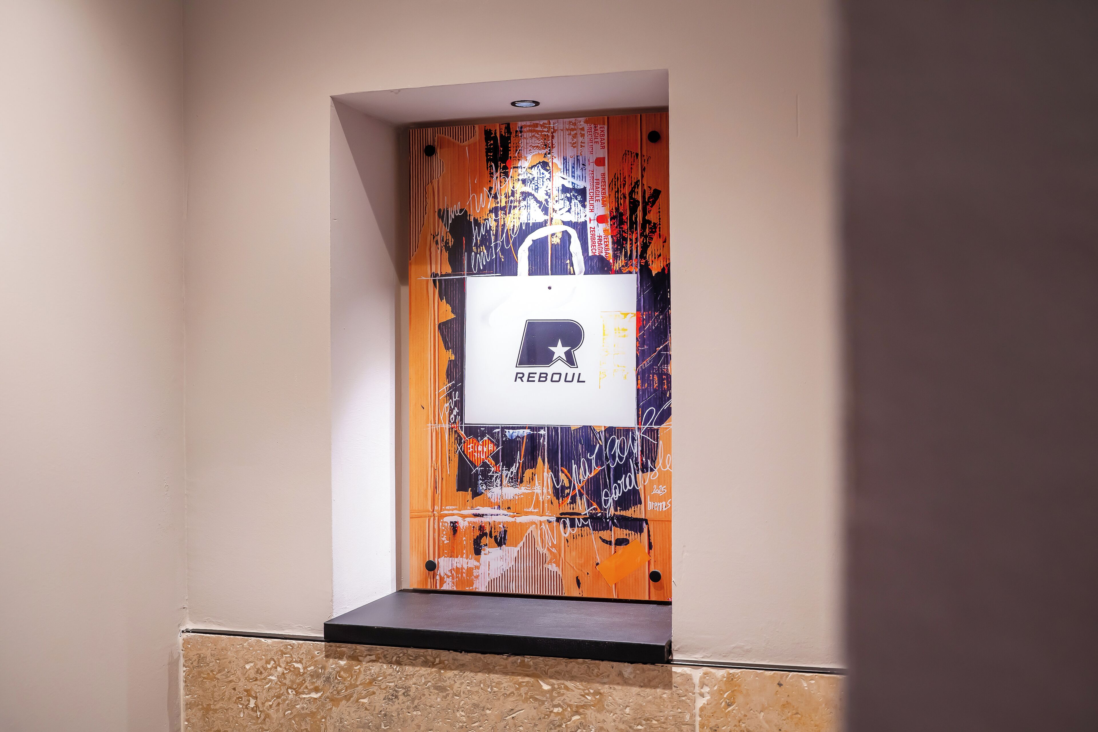 Een lift met een muur vol graffiti en een bord waarop 'REBOUL' staat.