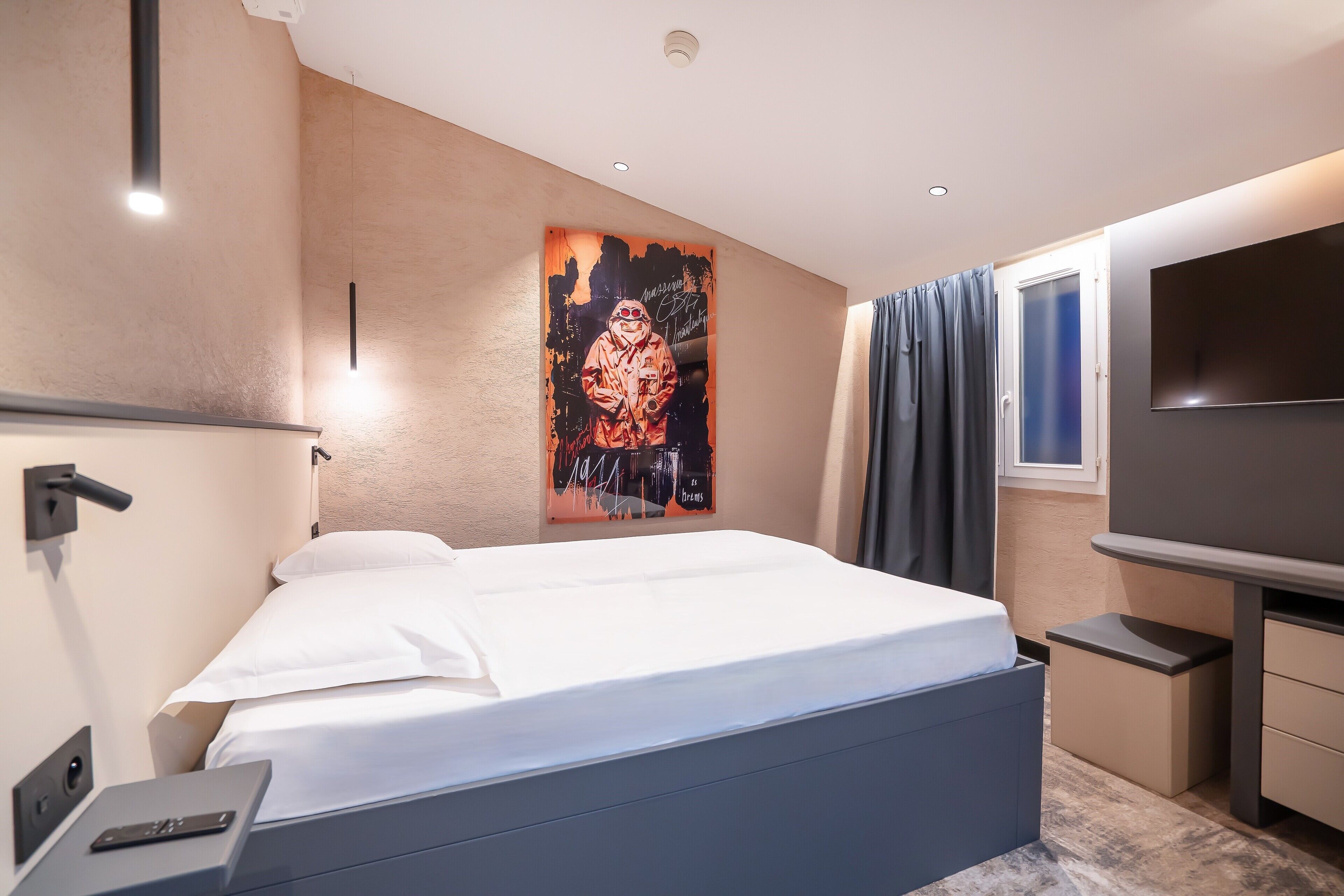 Ein modernes Hotelzimmer mit einem großen Bett, einem Flachbildfernseher, einem kleinen Schreibtisch und einem Poster an der Wand.