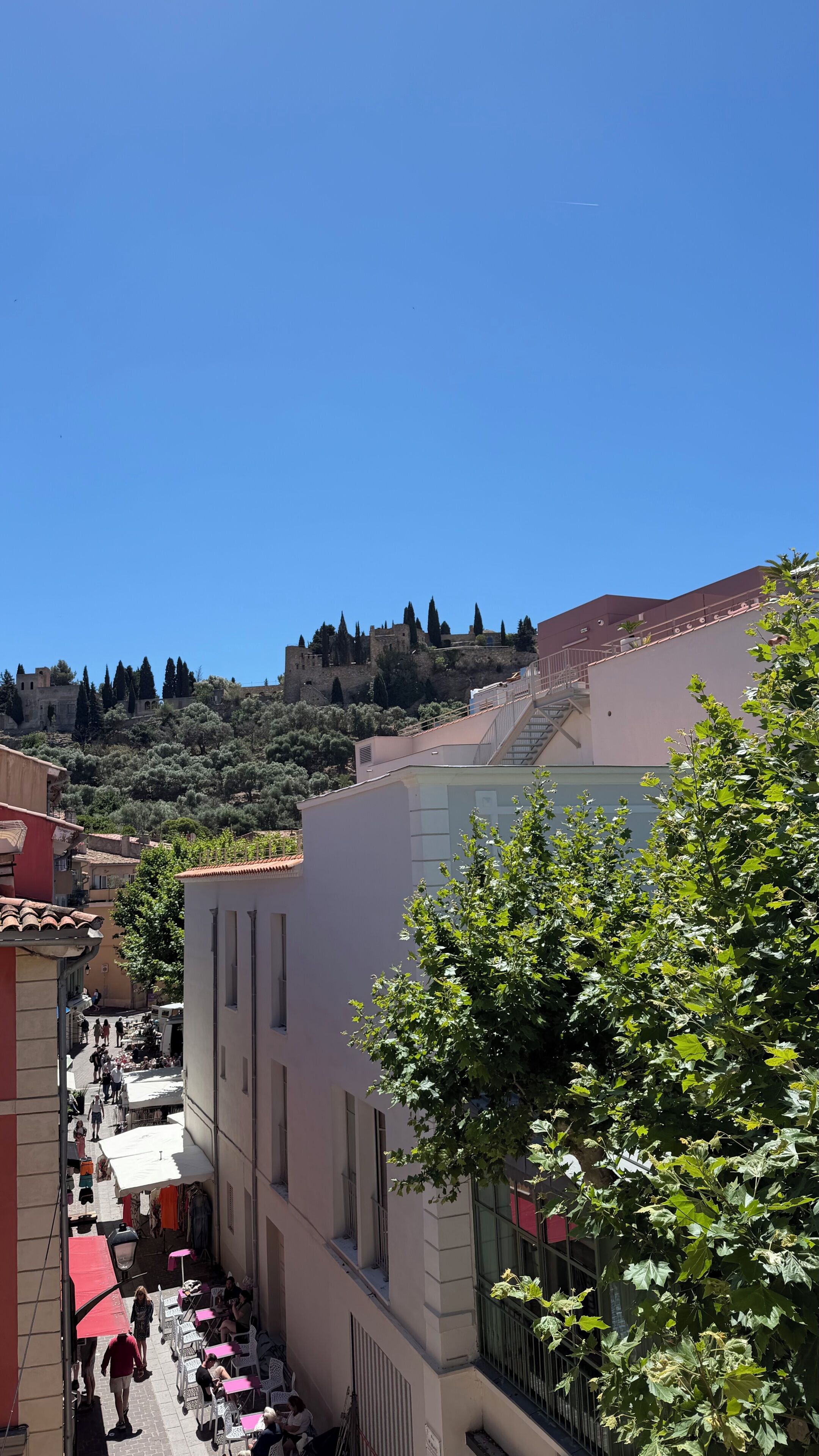 Vista de una calle con edificios, una escalera y una colina con árboles y una estructura que parece un castillo al fondo.