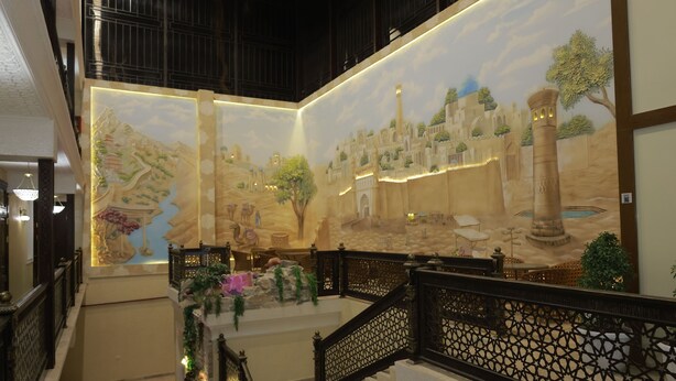 A grand staircase with ornate railings leading to a lobby area featuring a large mural depicting a historical scene. - Silk Road Terrace  (Bukhara)
