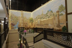 Una imponente escalera con barandales ornamentados que conduce a un vestíbulo con un gran mural que representa una escena histórica.