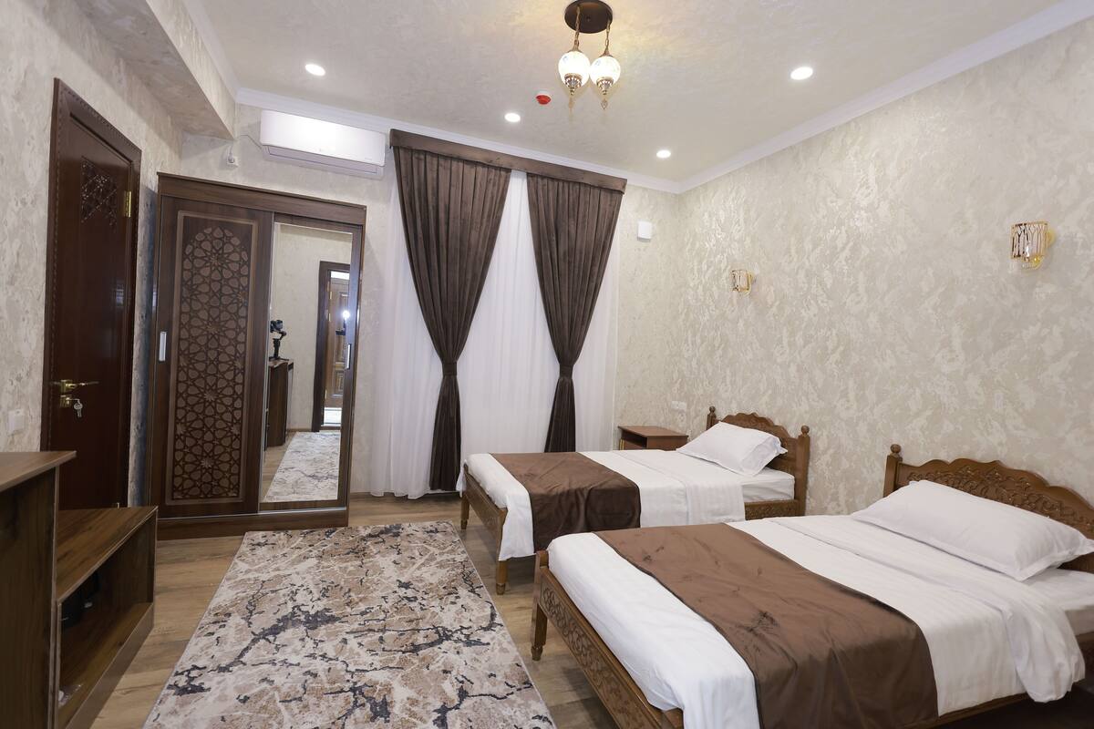 Une chambre d’hôtel avec deux lits, un grand miroir, une armoire en bois et un tapis à motifs.