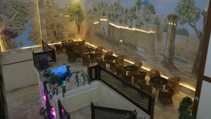 A restaurant with a desert-themed mural, wicker furniture, and a small indoor garden. - Silk Road Terrace  (Bukhara)