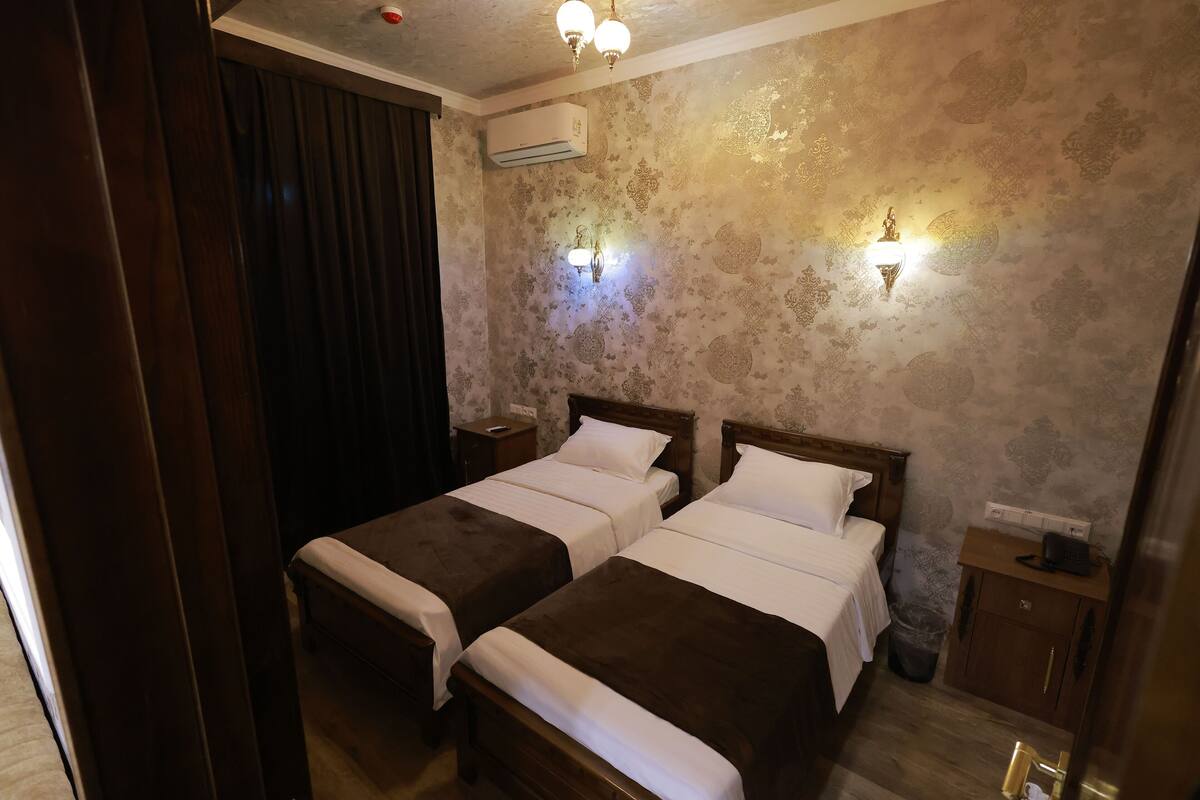 Une chambre d’hôtel avec deux lits, une tête de lit en bois, un climatiseur, une table de chevet et un petit placard.