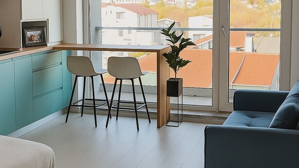En moderne lejlighed med et køkken, spiseområde og opholdsstue. Den har et stort vindue med udsigt over byen, en hængende lampe og en potteplante.