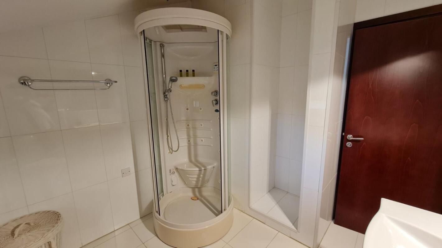 A bathroom with a glass-enclosed shower, a wooden door, and a towel rack.