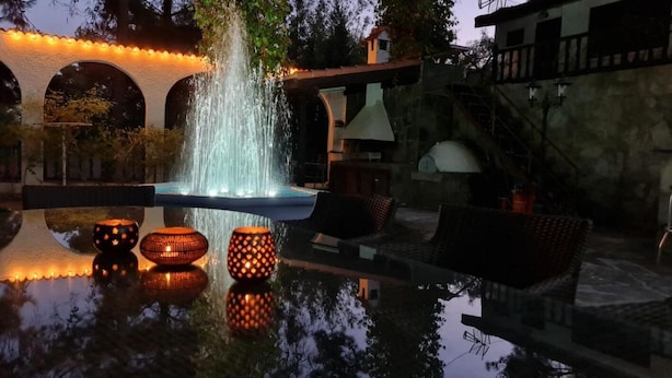A fountain with water jets, a pool reflecting the lights, and a seating area with chairs and tables. - Charming Villa in Moniatis, Cyprus - Private Pool & Garden (Saittas)