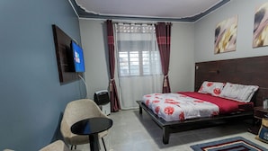 A bedroom with a bed, a chair, a TV, and a window with curtains. - The Den Soroti Red (Soroti)
