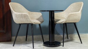 Two beige chairs with black legs and a black table in front of a blue wall. - The Den Soroti Red (Soroti)