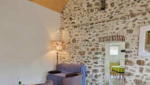 Una habitación con paredes de piedra, un sofá, dos sillones, una lámpara y una pequeña mesa con una planta.