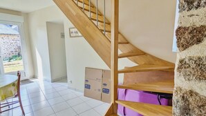 Una escalera con peldaños de madera y barandillas de metal, que conduce a una habitación con paredes blancas y piso de baldosas.