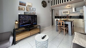Ein modernes Wohnzimmer mit Flachbildfernseher, einem Essbereich mit Tisch und Stühlen sowie einer Küche mit Herd und Schränken.