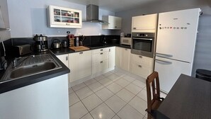 Eine moderne Küche mit weißen Schränken, einer schwarzen Arbeitsplatte, einer Edelstahl-Dunstabzugshaube, einer Mikrowelle, einem Backofen und einem Kühlschrank.