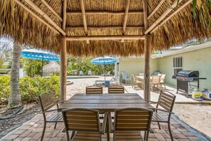 A covered patio with a table and chairs, a barbecue grill, and a pool in the background.