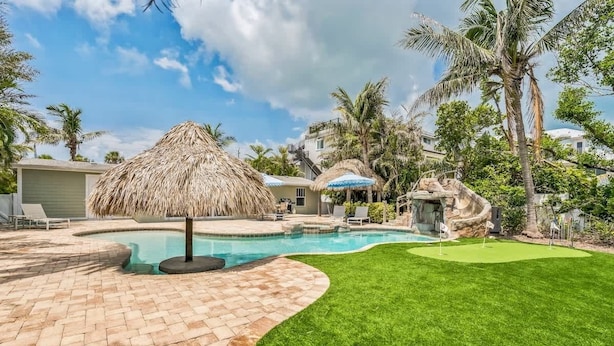 Un patio trasero con piscina, una sombrilla de paja y una formación rocosa.