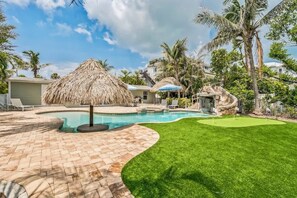 A backyard with a swimming pool, a thatched umbrella, and a rock feature.