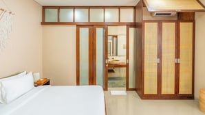 Ein Schlafzimmer mit Bett, Kleiderschrank und einem durch eine Glastür sichtbaren Badezimmer.