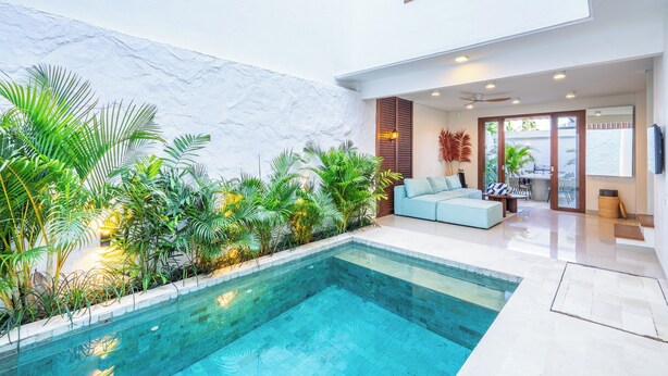 Ein moderner Poolbereich im Innenbereich mit klarem Becken, umgeben von üppiger Bepflanzung und einer Sitzecke mit Sofa und Tisch.