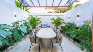 Eine Terrasse im Freien mit einem großen Tisch und Stühlen, umgeben von üppigem Grün und einer Pergola.