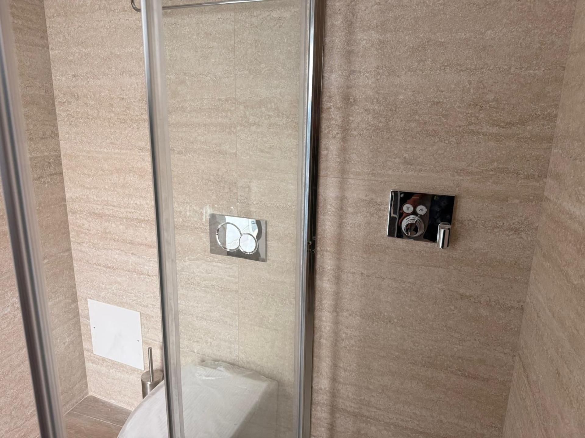 A bathroom with a glass shower enclosure, a towel rack, and a wall-mounted control panel.