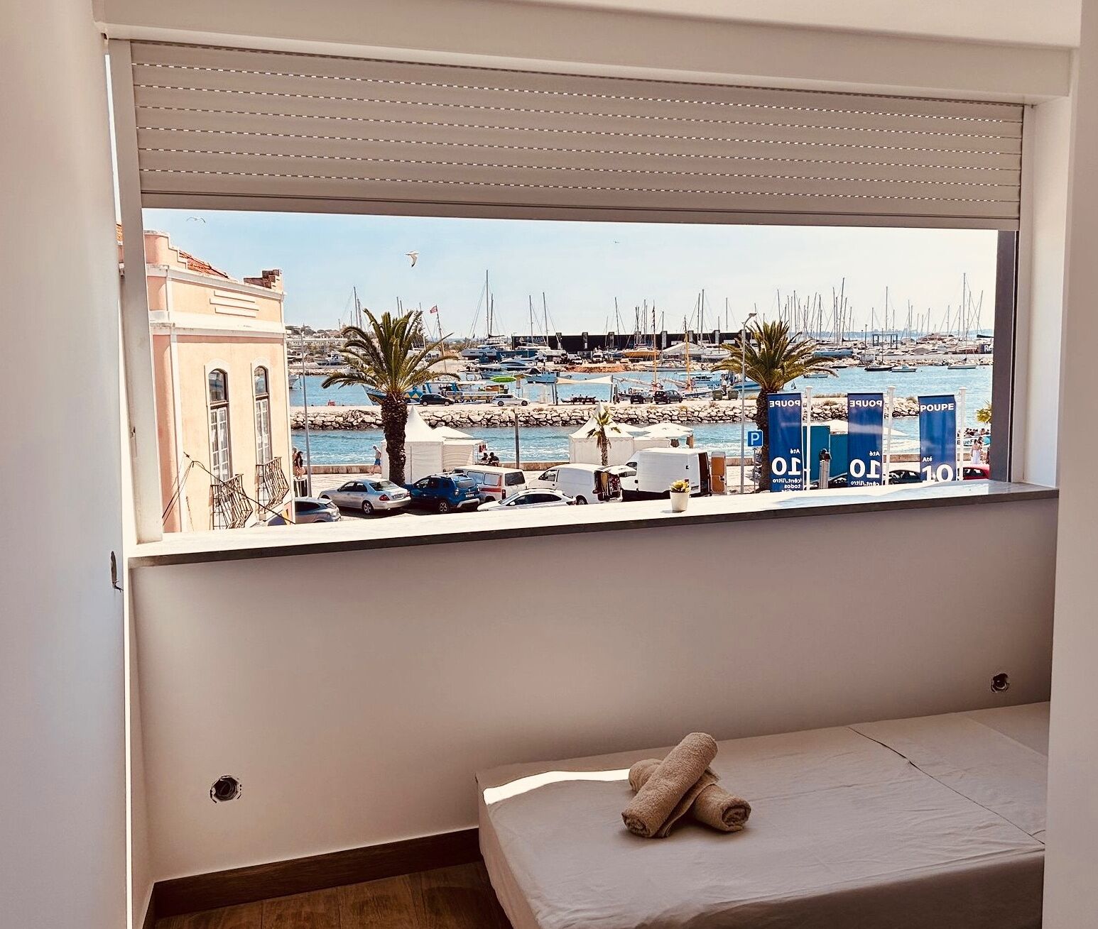 Une chambre avec une grande fenêtre donnant sur une marina, où l’on peut voir des bateaux et, au loin, un bâtiment.
