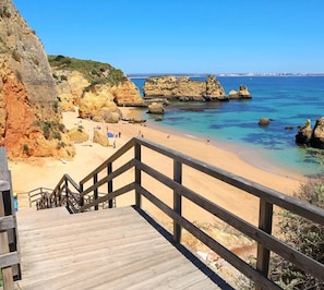 A wooden staircase leading to a beach with clear blue water and rocky formations. - Lagos Marina- Excellent Location- Close To Beach (Lagos)