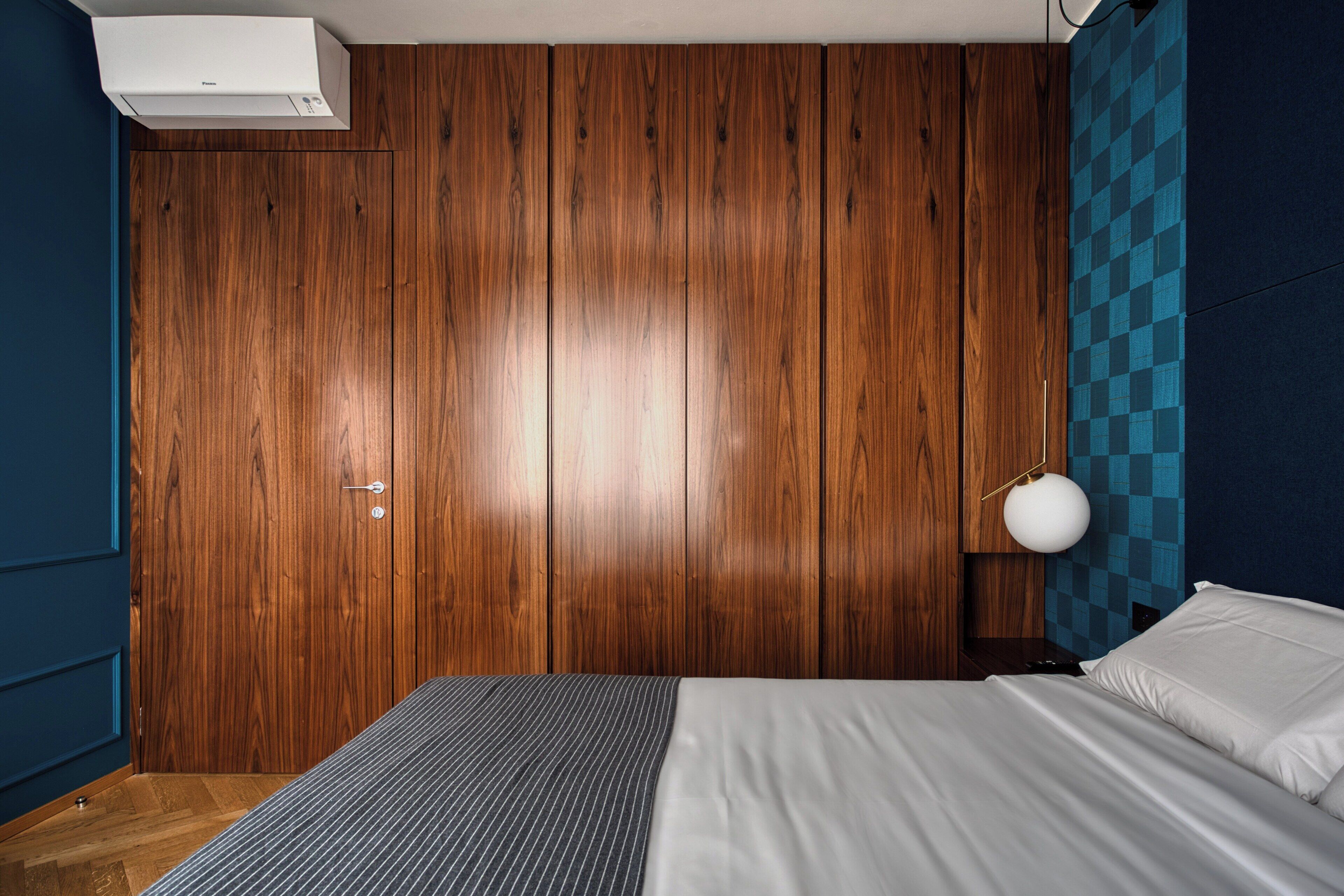 Ein Schlafzimmer mit einem Holzschrank, einem Bett mit weißer Bettwäsche, einer blauen Wand und einer Wand mit Karomuster.
