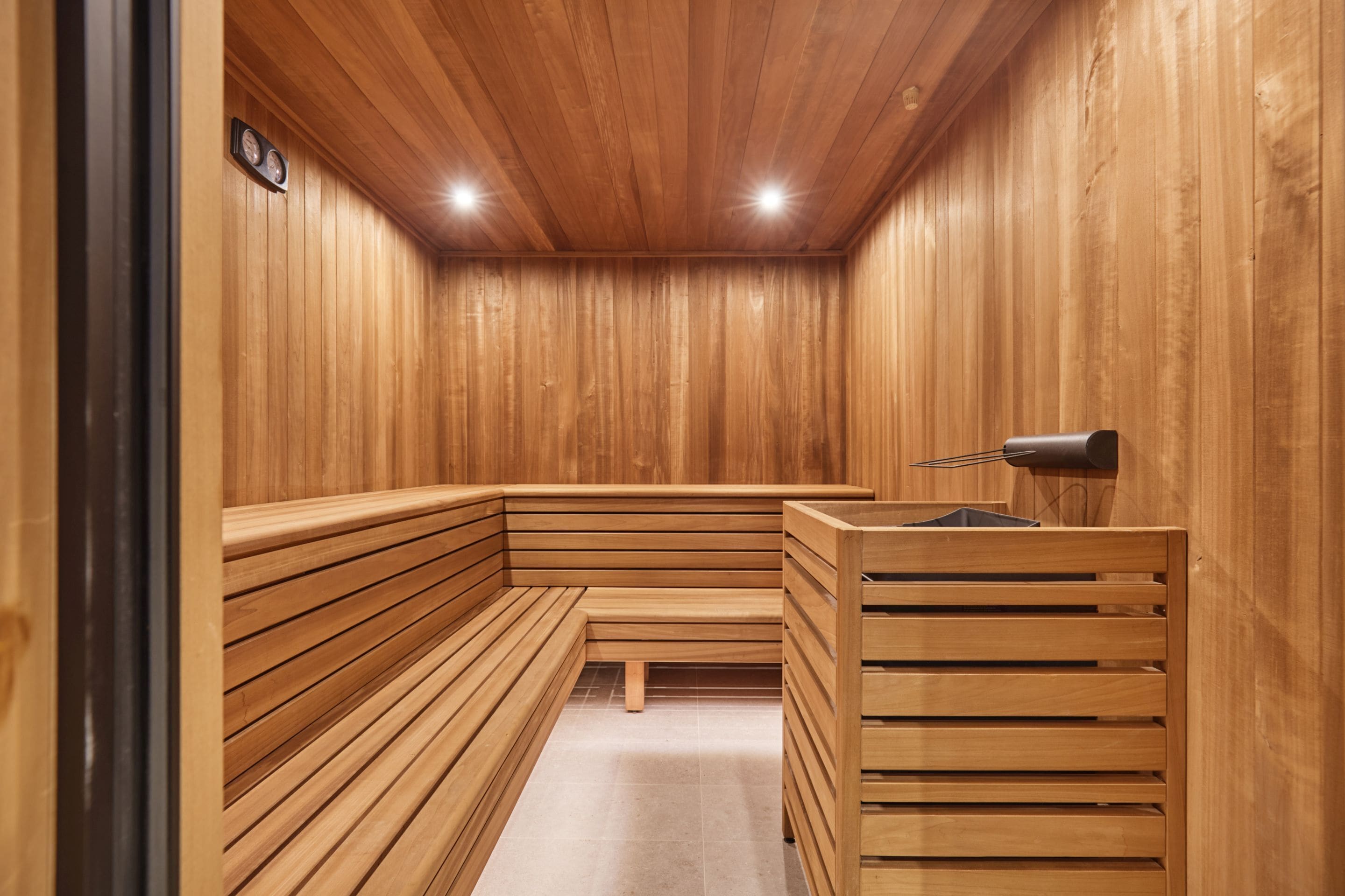 A wooden sauna with benches and a bench seat, a small table, and a wall-mounted clock.