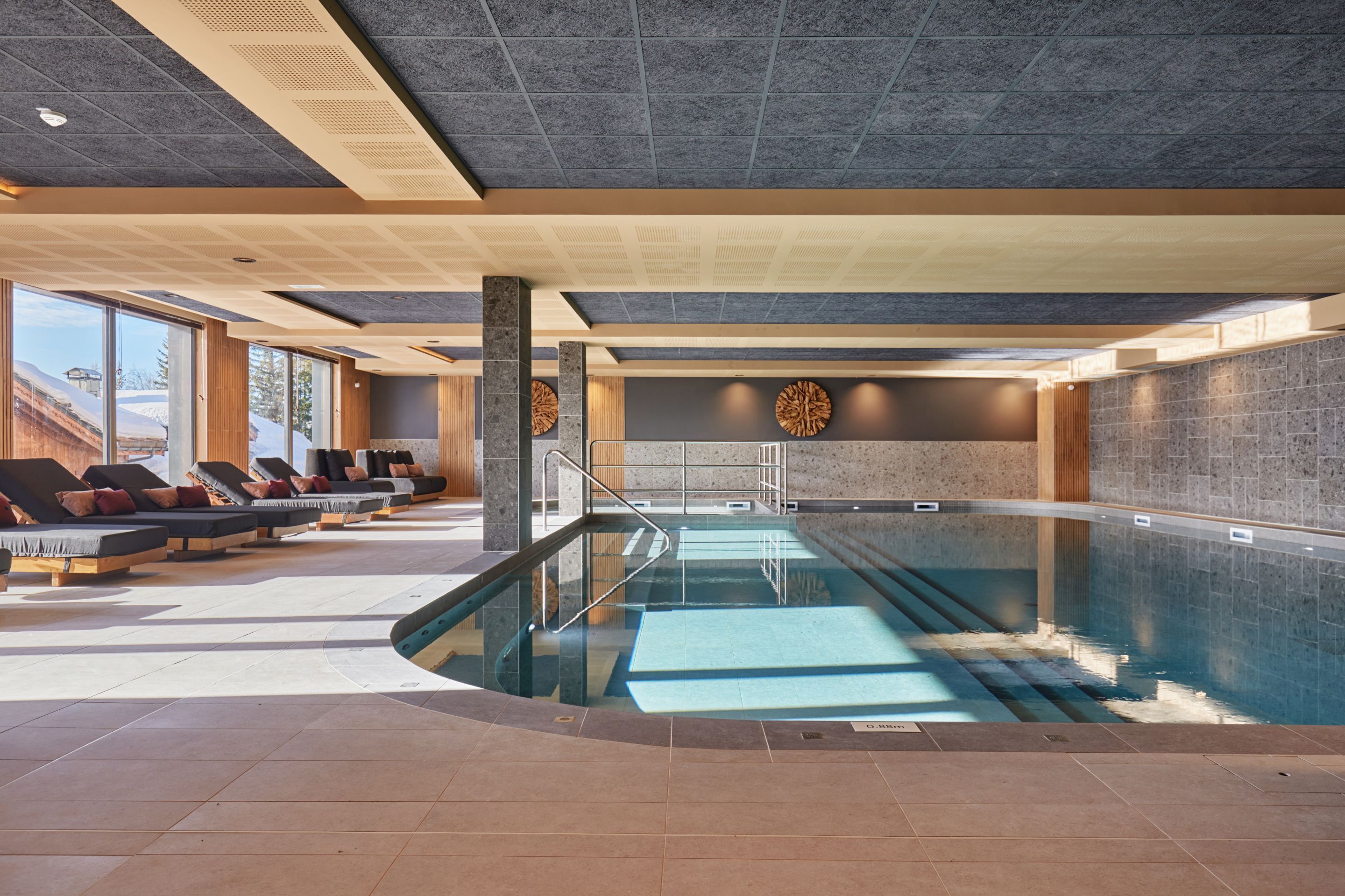 A modern indoor pool area with lounge chairs, a pool, and a view of the outdoors.