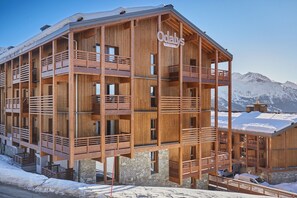A wooden multi-story building with balconies, named 'Odalys', set against a snowy mountain backdrop.
