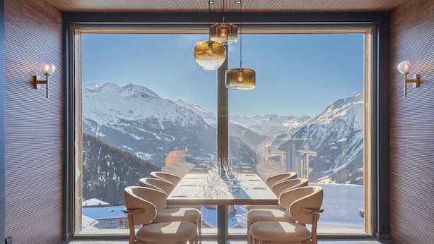 A dining area with a table set for six, facing a large window with a mountain view.