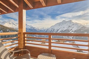 A wooden balcony with a view of snow-covered mountains and a clear sky.