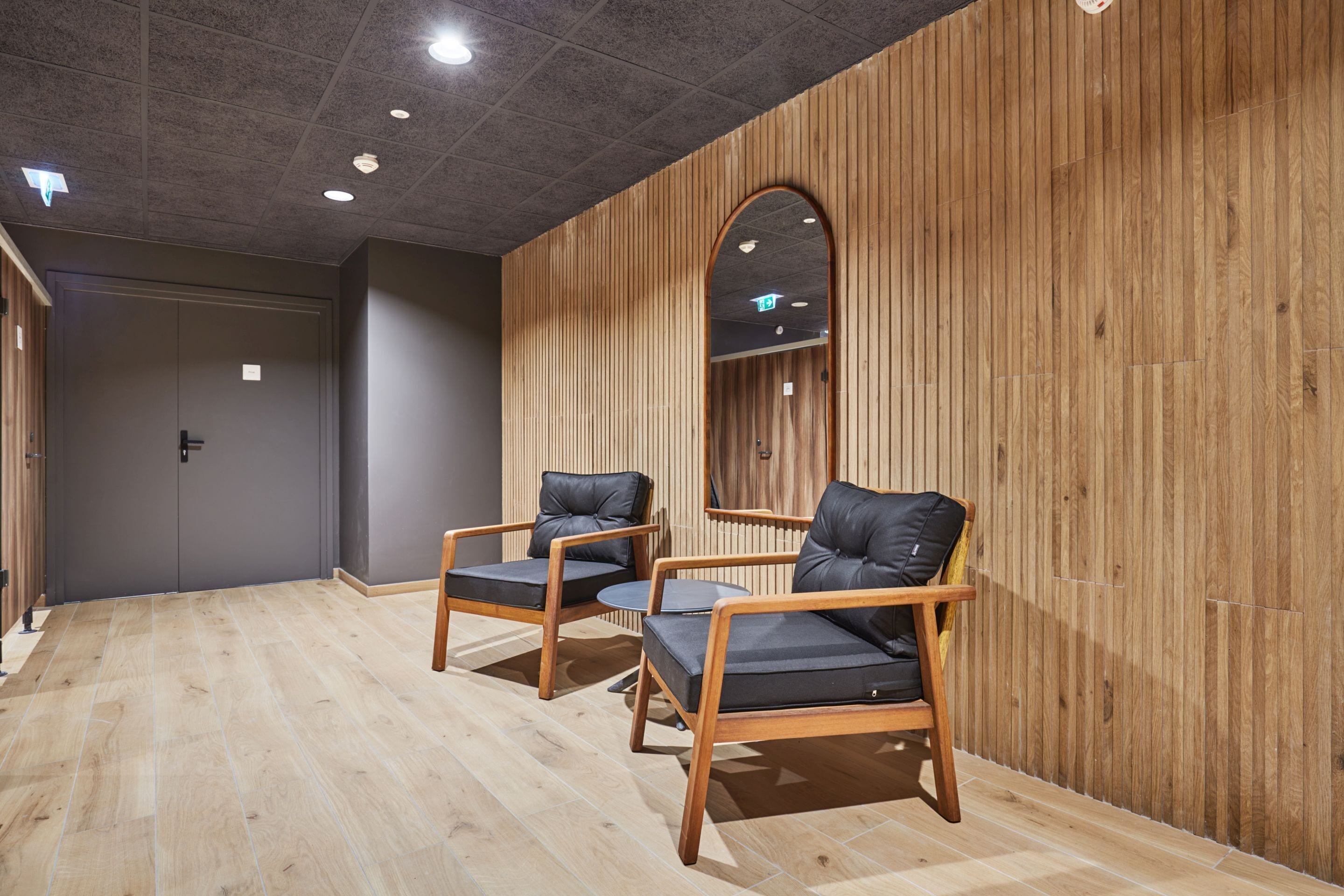 A room with two leather chairs, a wooden wall, and a ceiling with recessed lighting.
