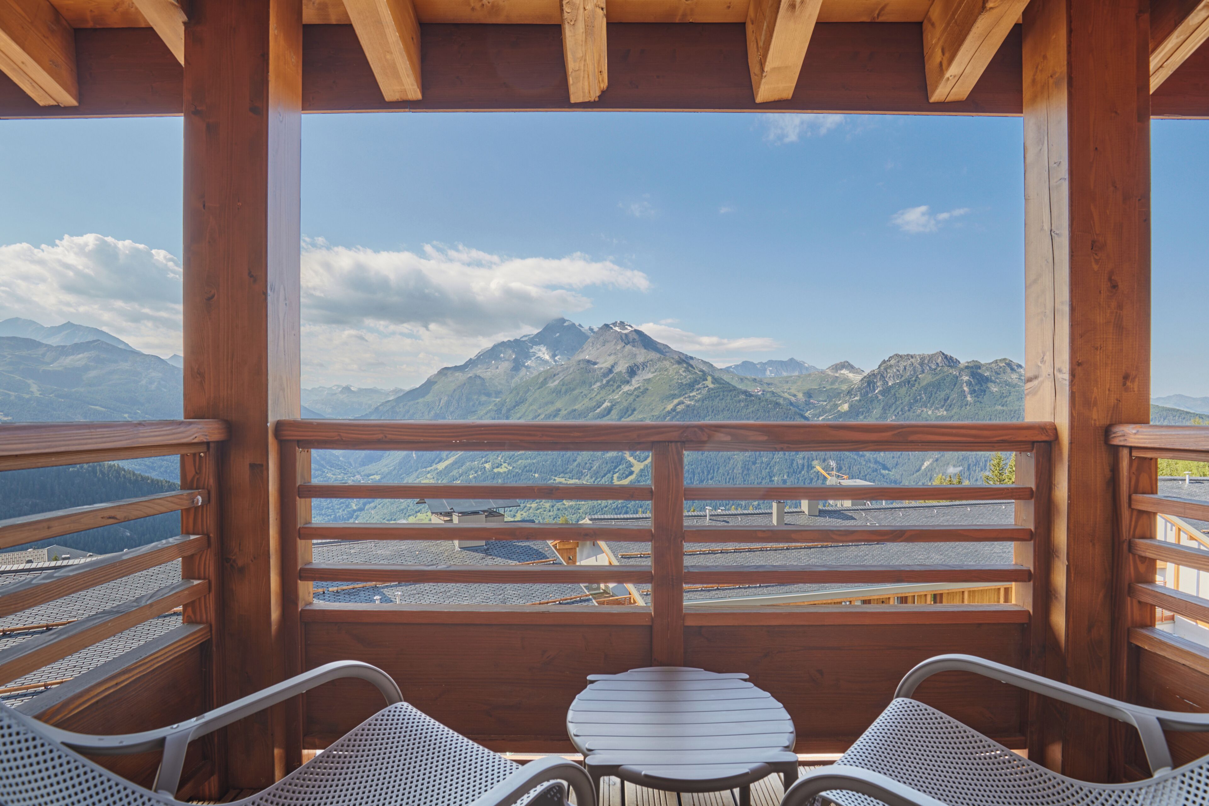 Un balcon en bois avec une table et deux chaises, donnant sur un paysage montagneux.
