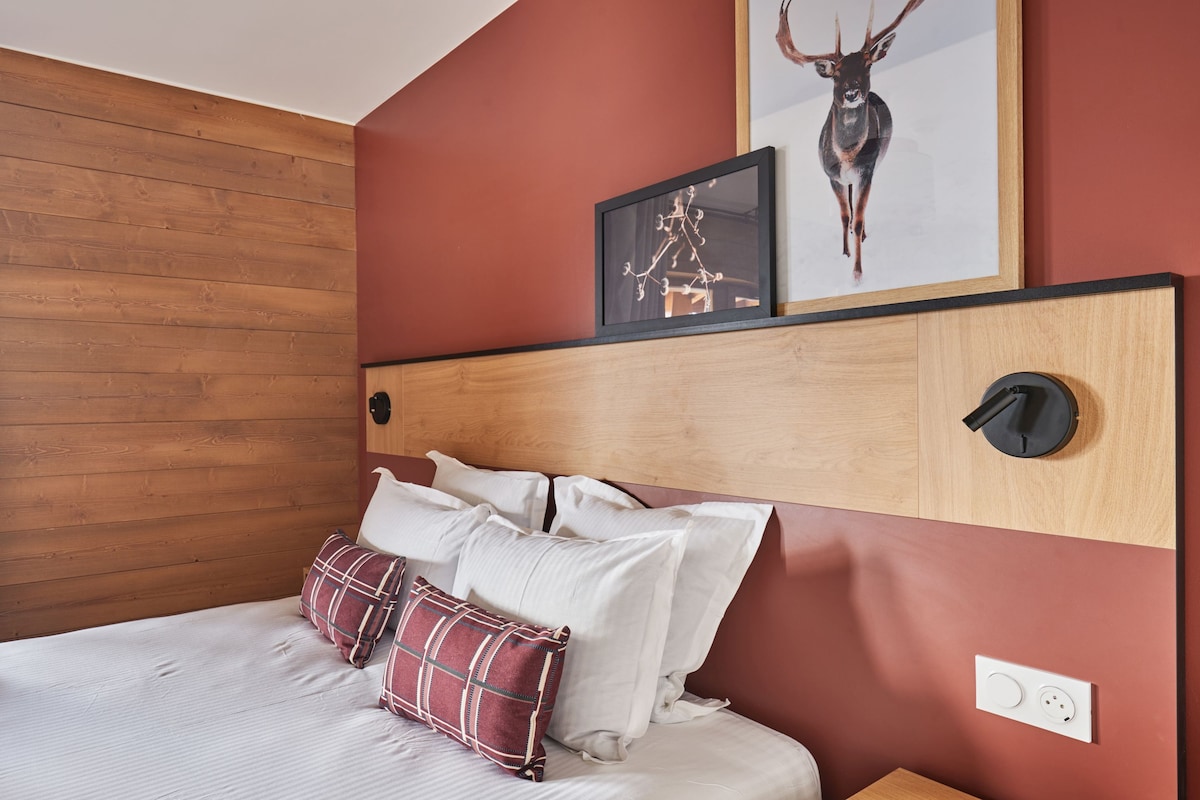 A bedroom with a wooden headboard, a bed with white bedding and plaid pillows, and two framed pictures on the wall.