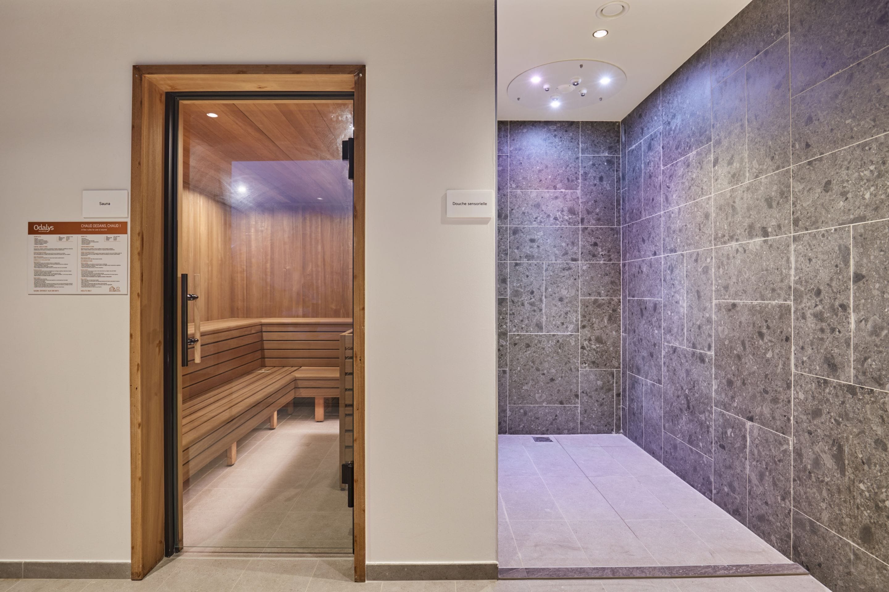 Un espace avec des bancs en bois, un mur recouvert de carreaux et un panneau indiquant la présence d’un sauna.