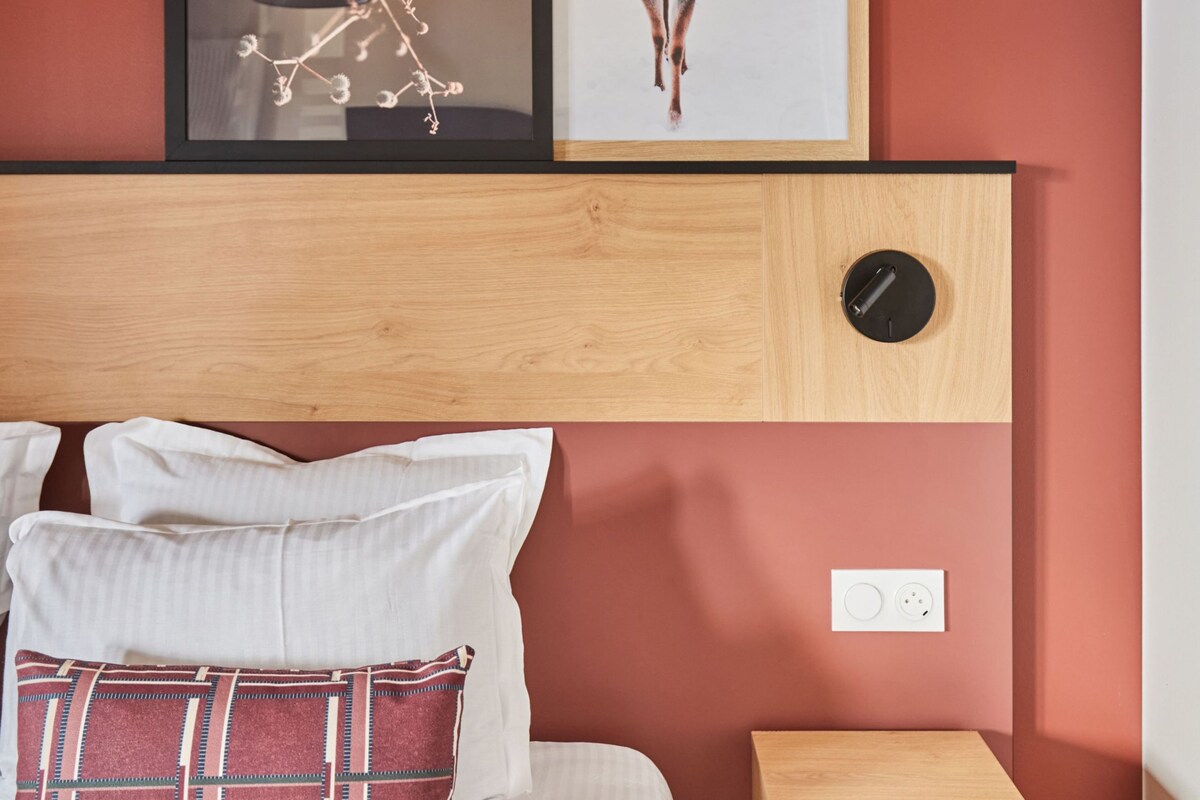 Un dormitorio con una cama, almohadas, una mesita de noche, un cabecero de madera, una obra de arte con ciervos enmarcada y una obra de arte abstracta enmarcada.