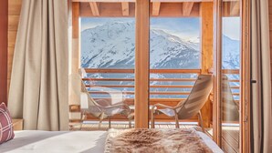 A room with a bed, two chairs, a window with a mountain view, and wooden walls.