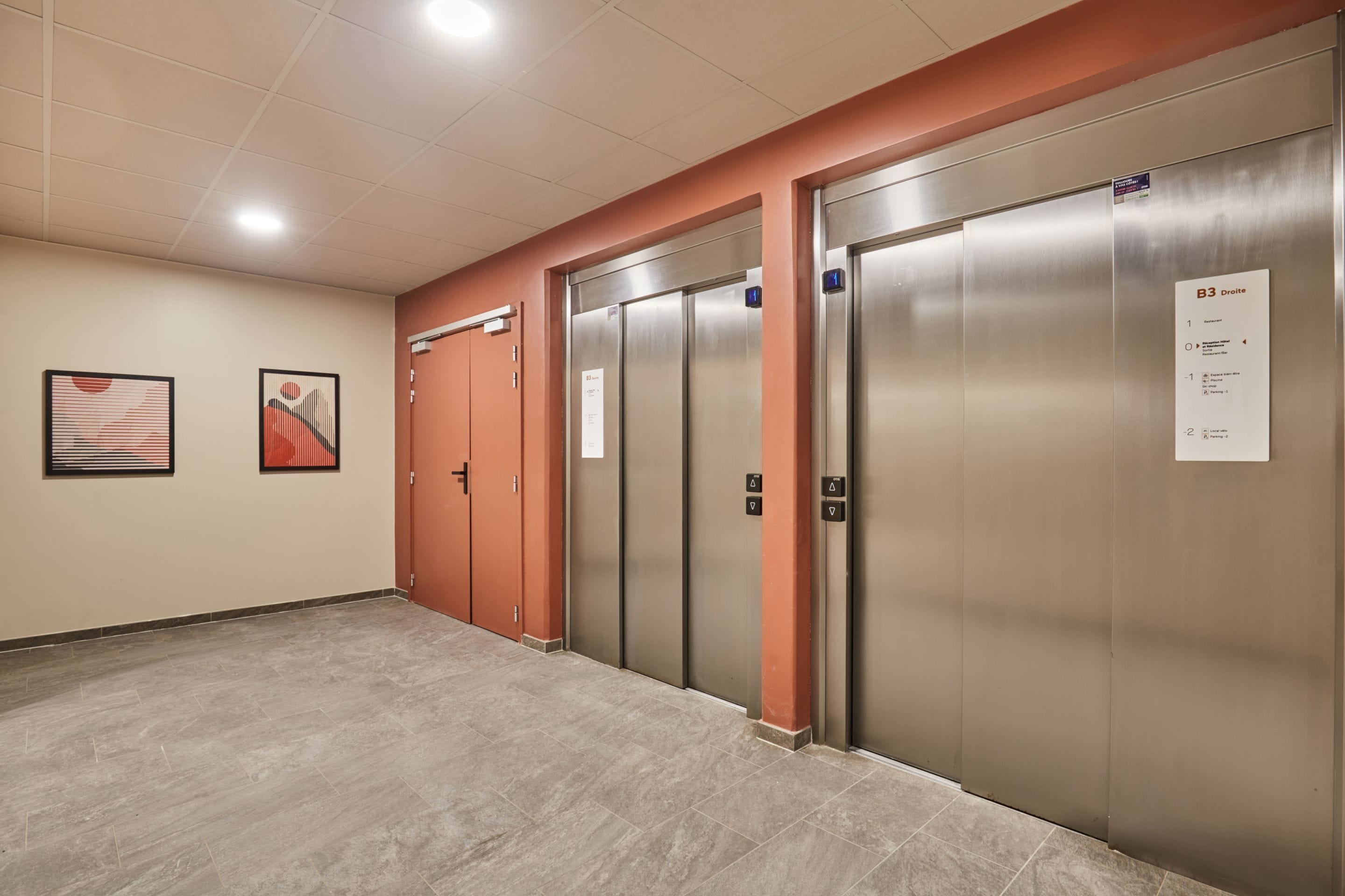 An elevator area with three elevators, a corridor, and two framed artworks on the wall.