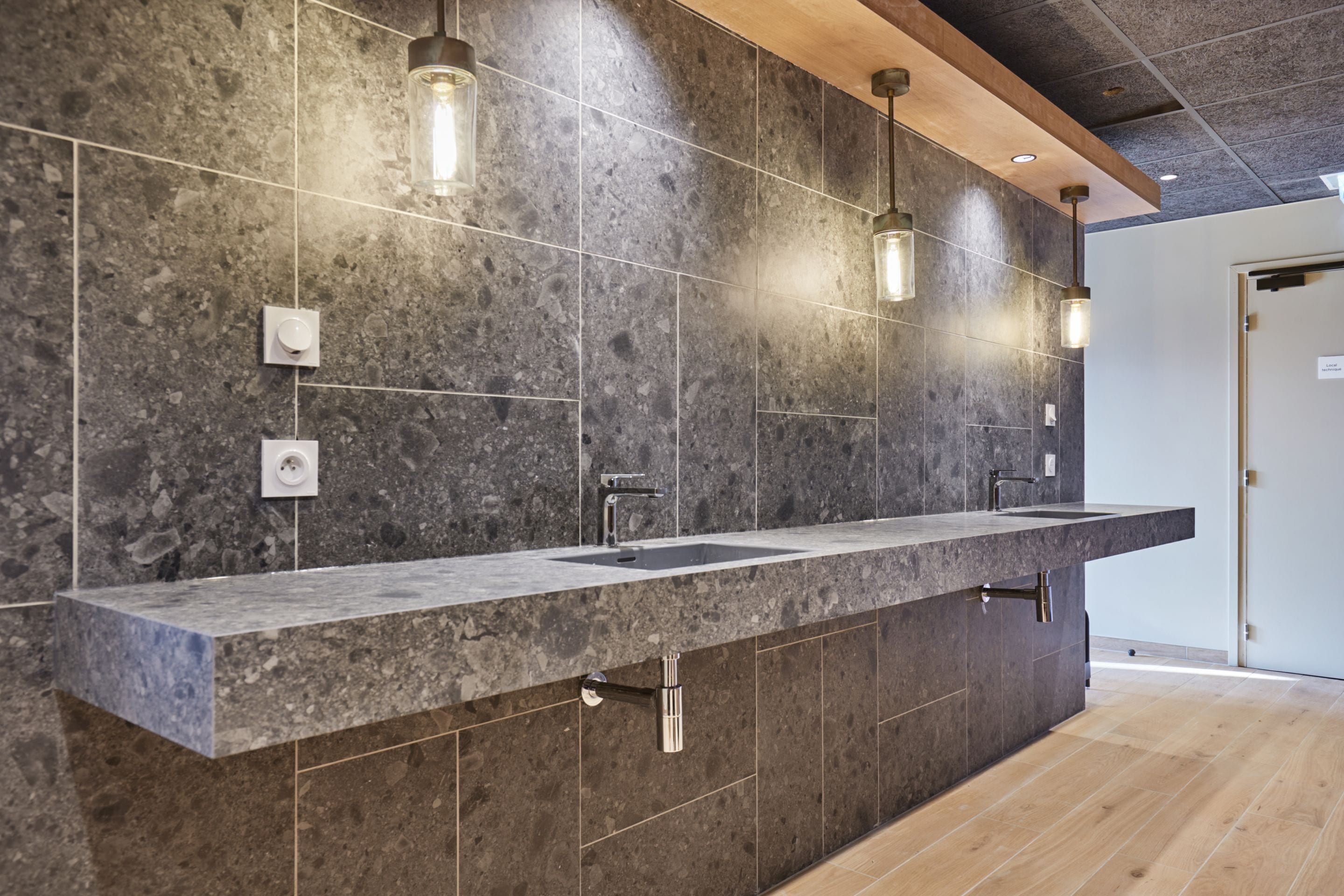 A modern bathroom with a long countertop, two sinks, and pendant lights.