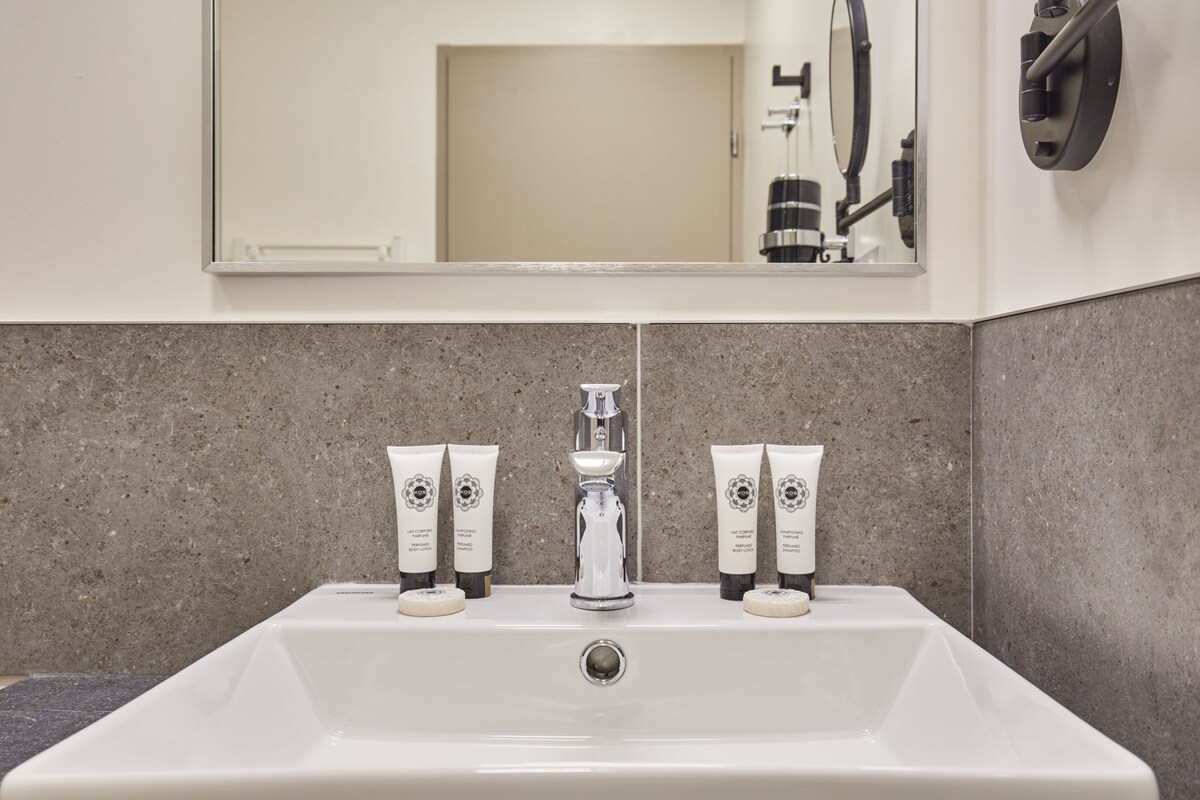 A bathroom with a white sink, a mirror, and three Kos body care products on the countertop.