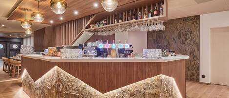 Zona de bar con mostrador de madera, luces colgantes y una variedad de botellas y vasos.