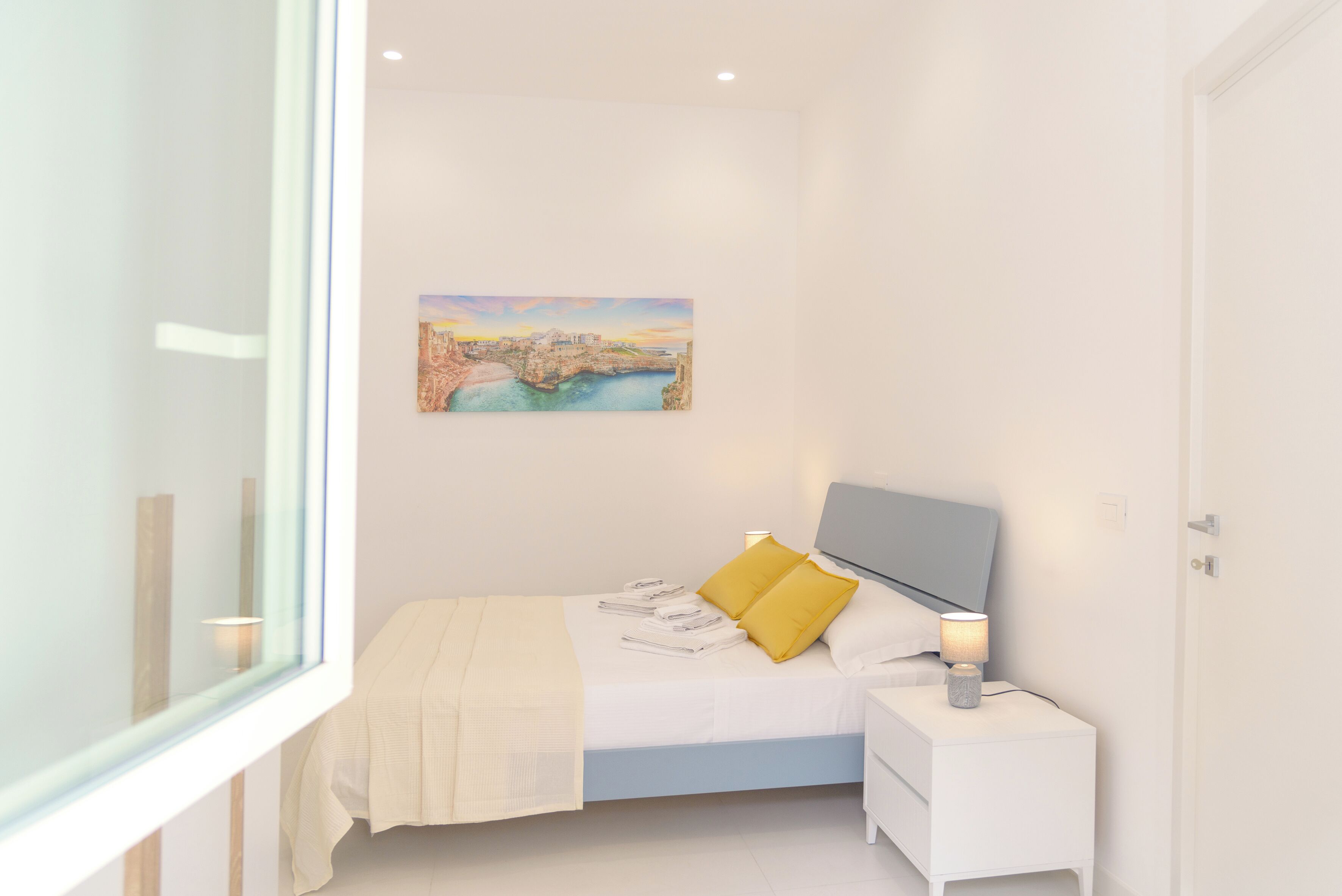 A modern bedroom with a bed, a nightstand, a lamp, and a painting on the wall.